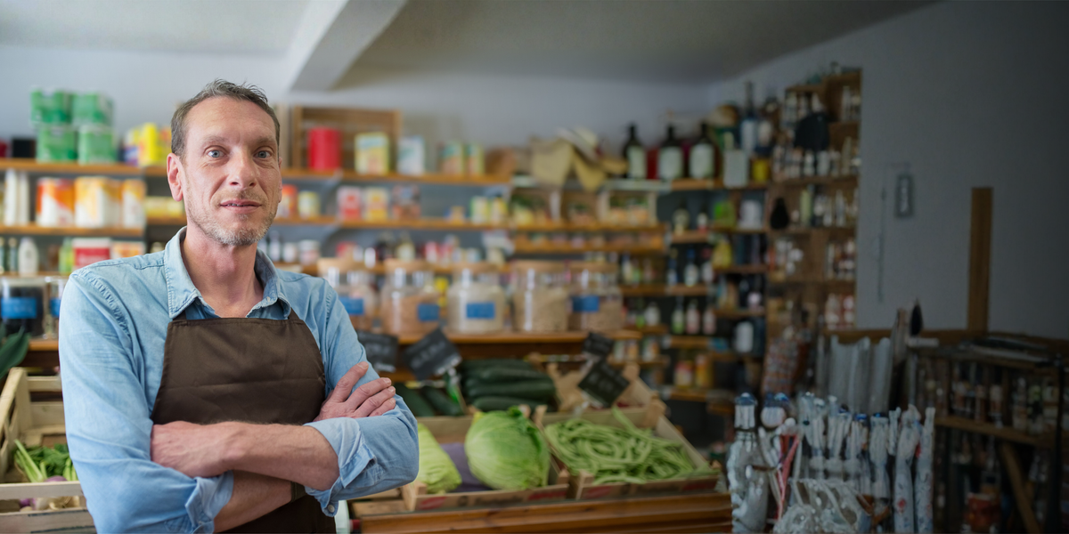 Winkelier voor de gevulde schappen van zijn buurtwinkel